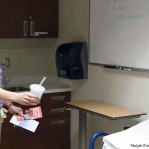 Photo of nurse handing cup of water to patient sitting on exam bed